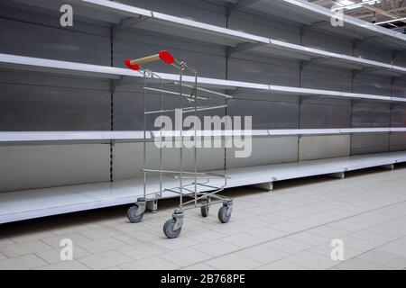 scaffali vuoti e carrello spesa in supermercato, tutto esaurito a causa del panico causato da epidemia di virus Foto Stock