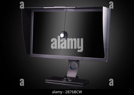 Monitor professionale con paraluce e calibratore isolato su nero Foto Stock