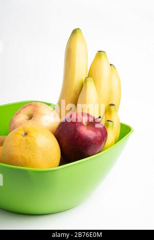 Una ciotola di plastica verde brillante con frutti freschi e maturi artfully arrangiati come mele, banane, arance ed altri regolato su un fondo bianco normale. Foto Stock