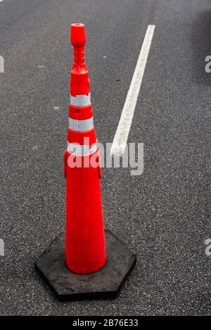 Grande cono di traffico arancione sul percorso con una linea guida bianca e uno sfondo di asfalto di strada Foto Stock