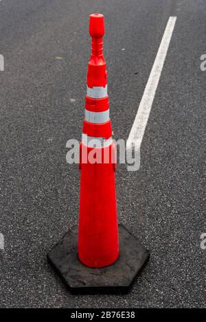 Grande cono di traffico arancione sul percorso con una linea guida bianca e uno sfondo di asfalto di strada Foto Stock