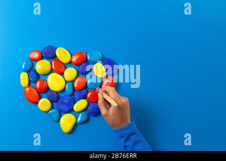 Giornata mondiale di consapevolezza dell'autismo. Pittura a mano di capretto con cuore di pennello fatto di pietre nei colori blu rosso giallo Foto Stock