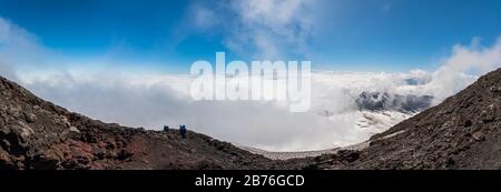 Paesaggio sul vulcano attivo Villarrica vista con un cielo nuvoloso dall'alto con neve e rocce con un gruppo di persone che discendono Foto Stock