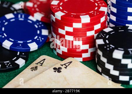 Un paio di assi, Club e Spade, su un mazzo di carte da gioco d'epoca ben utilizzato, circondato da chip scommesse blu, rossi e neri su un feltro verde standard Foto Stock