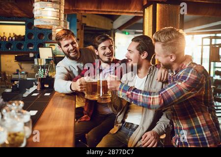 Amici con bicchieri di birra che si graffetta mentre si sta in piedi in un bar in un pub bar. Foto Stock