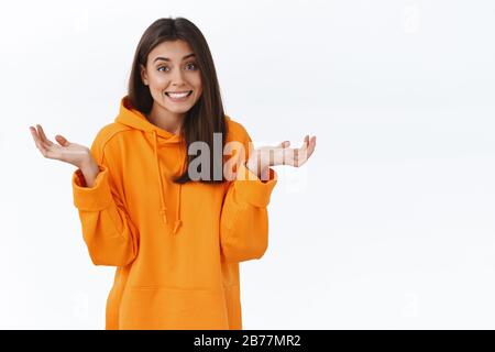 Scusa non lo so. Sorridente giovane bruna sciocca ragazza in piedi non importunata, scusandosi per essere incapace di aiuto, shrugging con le mani sparse lateralmente e. Foto Stock