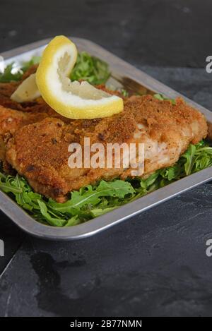 Bistecca di pollo impanata e fritta con una fetta di limone su un letto di insalata fresca - shot verticale studio Foto Stock