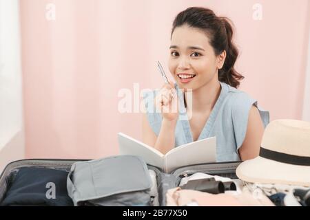 È meglio scrivere tutto! Giovane donna in una stanza luminosa davanti ai vestiti pensa che cosa altro deve essere piegato in una valigia prima del viaggio Foto Stock