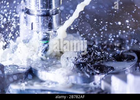 Vista ravvicinata del processo di fresatura verticale in acciaio cnc con flussi di liquido di raffreddamento dell'acqua esterni, schizzi e molti trucioli metallici, contrasto elevato Foto Stock