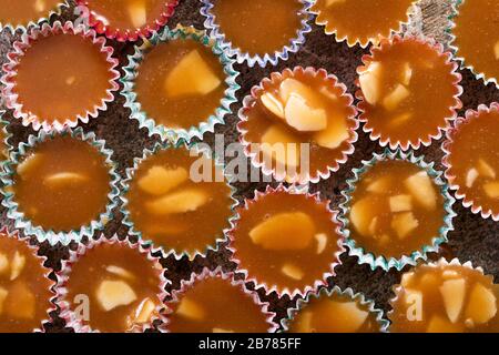 Caramelle al butterscotch svedesi knäck con mandorla, in piccole tazzine di carta multicolore. Primo piano su una superficie di pietra grigia. Visto dall'alto, macro pho Foto Stock