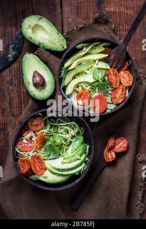 Insalata sana con spaghetti di zucchine, pomodori arrostiti al forno e avocado. L'insalata è vista dall'alto, e viene servita in ambiente riciclato Foto Stock