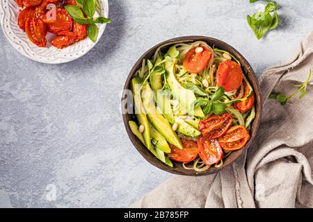 Insalata sana con spaghetti di zucchine, pomodori arrostiti al forno e avocado. L'insalata è vista dall'alto, e viene servita in ambiente riciclato