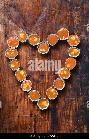 Caramelle al butterscotch svedesi knäck a forma di cuore, su un rustico sfondo di tavola in legno. La caramella è avvolta in carta colorata piccola Foto Stock