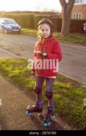 Bambina di dieci anni in un casco, cuscini a gomito e ginocchiere pattinaggio all'aperto. Vacanze scolastiche primaverili. Messa a fuoco selettiva, luce del tramonto. Foto Stock