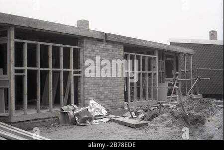 Fine degli anni '60, forse all'inizio degli anni '70, una nuova, moderna casa a un piano o bungalow in fase di costruzione, un mix di mattoni e legno incorniciato, su cui piastrelle saranno rivestite e prefatto finestre installati, Inghilterra, Regno Unito. Foto Stock