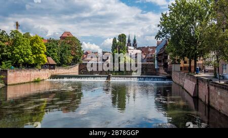 Norimberga 2019. Ponte massimo sul fiume Pegnitz visto tra gli alberi e le rive. Siamo in una giornata estiva soleggiata ma nuvolosa. Agosto 2019 a Nuremb Foto Stock