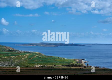 Una vista dal sentiero costiero dell'isola di Gozo alla piccola isola disabitata di Comino maltese; si possono vedere antichi forti costieri difensivi Foto Stock