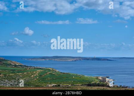 Una vista dal sentiero costiero dell'isola di Gozo alla piccola isola disabitata di Comino maltese; si possono vedere antichi forti costieri difensivi Foto Stock