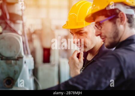 pensiero dei lavoratori, team di assistenza che lavora con la macchina insieme lavoro di squadra in stabilimento industriale pesante con casco di sicurezza. Foto Stock