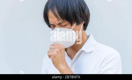 Un uomo asiatico indossa maschera N95 e tosse azione Foto Stock