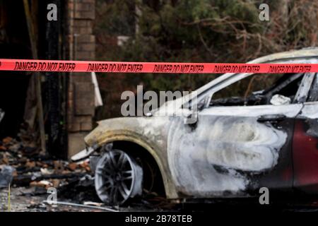 Incendio dell'automobile veicolo bruciato distrutto da un incendio di grandi dimensioni. Resti incendiati di un veicolo con nastro di reato dopo Arson. Macchina bruciata dopo il fuoco. Foto Stock