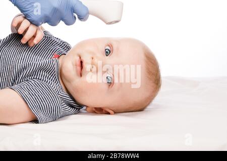 Il pediatra o l'infermiere controlla la temperatura corporea del bambino utilizzando un termometro frontale a infrarossi (termometro a pistola) per verificare l'eventuale presenza di sintomi di malattia Foto Stock