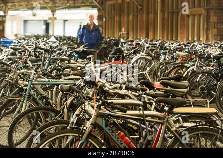 Un enorme numero di biciclette presso il parco ciclabile sulla piattaforma della stazione ferroviaria di Bristol Temple Meads, con un uomo in lontananza che le guarda Foto Stock