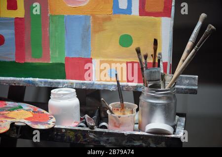 Set di materiali per pittura professionale, tra cui tavolozza di colori, giare con gouache e pennelli e cavalletto con foto Foto Stock
