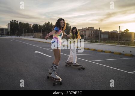 Inquadratura grandangolare di due ragazze su uno skateboard sotto un cielo nuvoloso Foto Stock