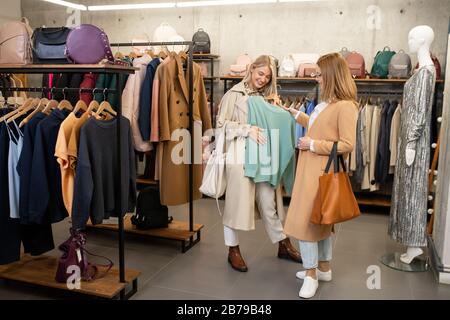 Giovane donna che mostra maglione di cotone blu chiaro al suo amico, mentre la scelta di nuovi vestiti nel centro commerciale durante lo shopping Foto Stock