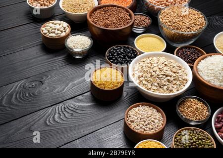 Vari Cereali, granaglie, semi, semole, legumi e fagioli in ciotole in legno nero con sfondo spazio copia Foto Stock