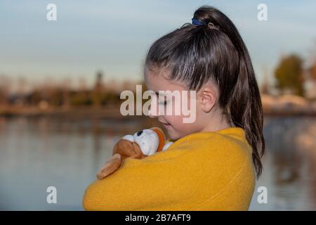 ragazza con un maglione giallo che abbracciano un teddy vicino a un lago . Concetto di amicizia, amore, tenerezza Foto Stock