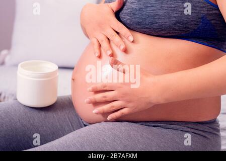 Donna incinta strofinando il ventre con lozione del corpo contro i segni di stiramento sulla pelle durante la gravidanza. Foto Stock