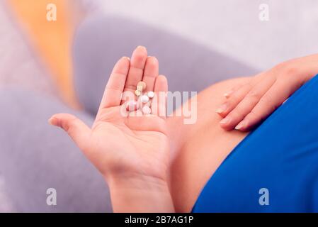 Vitamine durante la gravidanza. Donna incinta che tiene le pillole in mano ed espone il suo ventre. Foto Stock