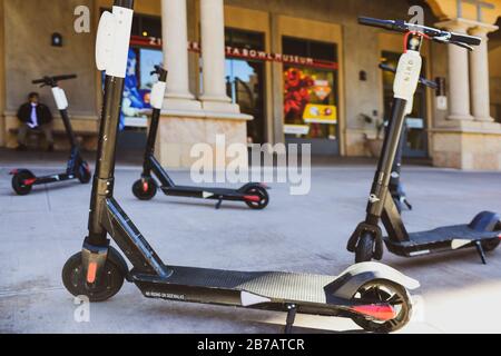 Un gruppo di scooter elettrici parcheggiati in modo casuale in affitto sul marciapiede di fronte a negozi, musei e condomini al Waterfront Scottsdale, Arizona Foto Stock