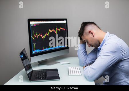 Uomo che lamenta con le mani sulla testa di fronte al computer con il grafico del business infruttuoso sullo schermo. Foto Stock