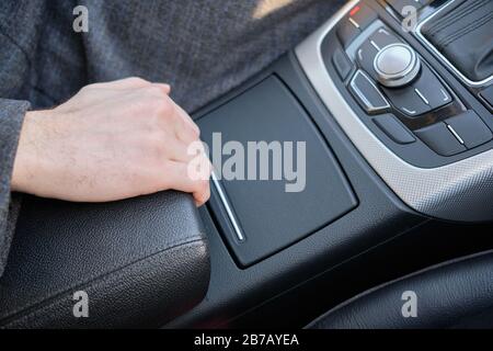 Un uomo in una macchina moderna. La mano solleva il bracciolo. Primo piano. Foto Stock