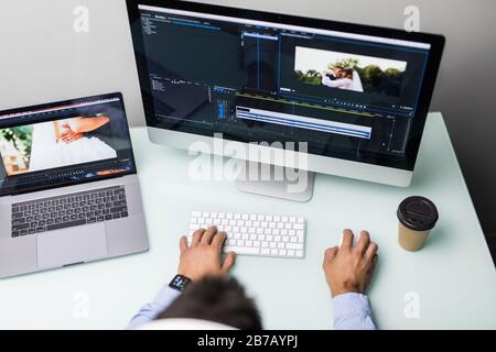 Visualizzazione ad angolo basso dell'editor video di un giovane uomo con opere con filmati sul suo personal computer con grande display in ufficio Foto Stock