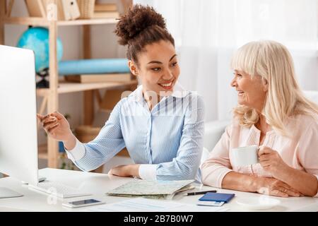 Discesa Africana donna agente di viaggio in ufficio mostrando prenotazione su computer a donna anziana sorridente gioioso Foto Stock