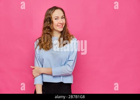 Elegante ragazza caucasica in una t-shirt blu pallido in posa per la fotocamera su uno sfondo rosa. Primo piano. Foto Stock