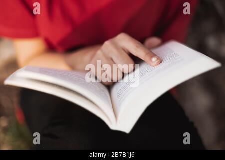 Primo piano di un libro aperto a destra nel mezzo da una giovane femmina che sta puntando il suo dito in una parola della pagina. Profondità di campo bassa. Foto Stock