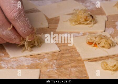 Una donna scolpisce gnocchi e ravioli da quadrati di pasta e cavolo. Pannello di taglio compensato, setaccio di farina di legno e perno di laminazione di legno - attrezzi per Foto Stock