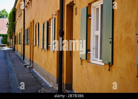 Augsburg, Germania: Pareti gialle di senape e finestre verdi chiuse dei Fuggerei. Il Fuggerei è il più antico complesso residenziale sociale del mondo. Foto Stock