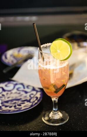 Un bordo salato su stemware offre un cocktail rosa fatto con cetrioli e lime con paglia in acciaio inossidabile sul tavolo del bistro all'esterno Foto Stock