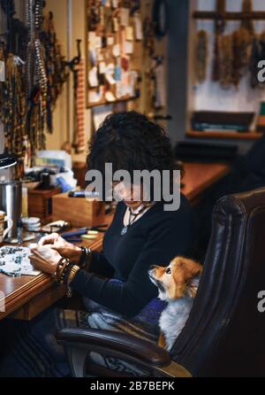 Bead artist Beverly Moore a jeweler banco di lavoro presso la sua boutique, 'Earthenrate', parlando con il suo piccolo cane sulla 5th Avenue nella città vecchia Scottsdale, Arizona, Foto Stock