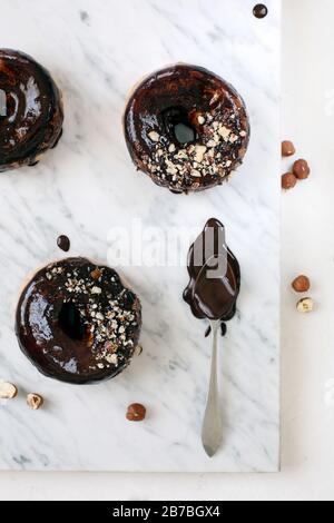 Ciambelle al cioccolato su fondo in pietra bianca, posa piatta Foto Stock