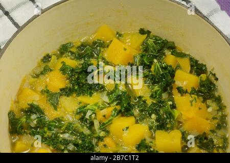 Closeup di kale caldo e di cubetti di zucca di butternut con cipolla tritata di scalogno in pentola su asciugamano piatto Foto Stock