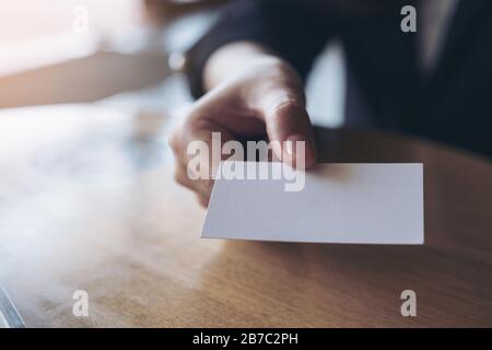 Donna d'affari che tiene e che dà un biglietto da visita vuoto a qualcuno sul tavolo in ufficio Foto Stock