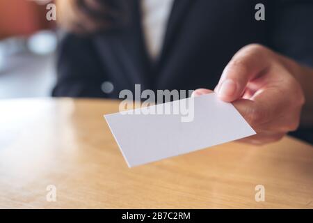 Donna d'affari che tiene e che dà un biglietto da visita vuoto a qualcuno sul tavolo in ufficio Foto Stock