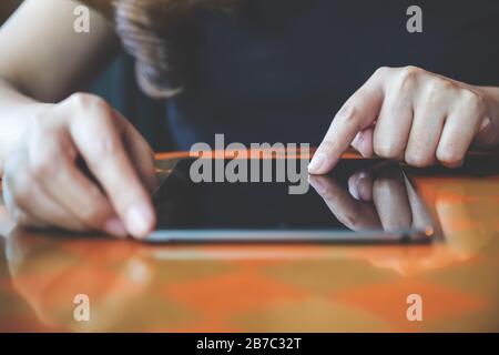 Immagine ravvicinata delle mani di una donna che puntano, toccano e usano un tablet pc sul tavolo in un bar Foto Stock